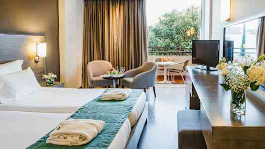 Hotellihuone, jossa parivuode, oleskelualue kahdella tuolilla ja pöydällä sekä parveke näkymällä. (Tekoälyn luoma teksti)