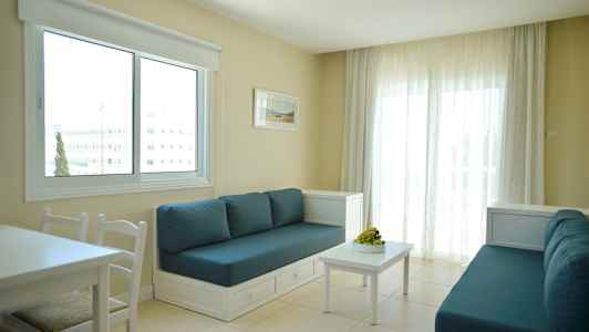 Huone, jossa kaksi sohvaa sinisillä tyynyillä, valkoinen pöytä ja suuri ikkuna vaaleilla verhoilla. (Tekoälyn luoma teksti)