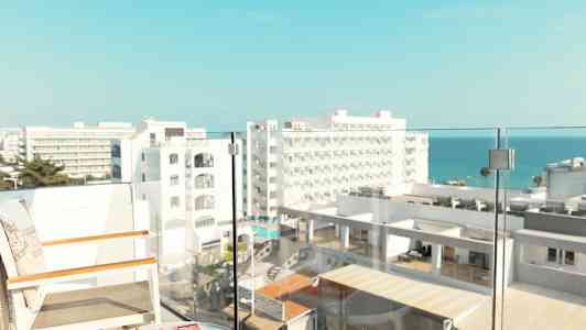 Näköala parvekkeelta, jossa on tuoleja ja pöytä, hotellirakennuksia ja meri taustalla. (Tekoälyn luoma teksti)