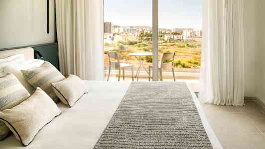 Hotellihuone, jossa parivuode ja pääsy parvekkeelle, jossa pöytä ja tuolit. (Tekoälyn luoma teksti)