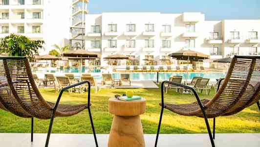 Kaksi tuolia ja pöytä terassilla, näkymä uima-allasalueelle ja hotellille. (Tekoälyn luoma teksti)