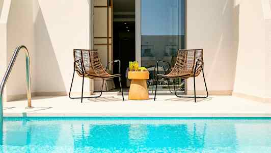 Kaksi tuolia ja pöytä, joilla on lasit, ovat uima-altaan äärellä oven edessä. (Tekoälyn luoma teksti)