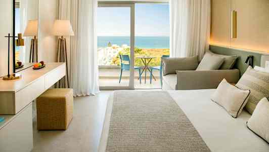 Hotellihuone, jossa on parivuode, istuinryhmä ja parveke, jolta on näkymä merelle. (Tekoälyn luoma teksti)