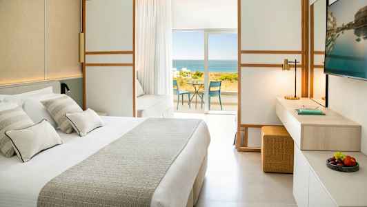 Hotellihuone, jossa on suuri sänky, televisio ja näkymä merelle parvekkeelta. (Tekoälyn luoma teksti)