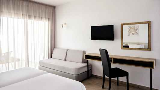 Hotellihuone, jossa on kaksi sänkyä, sohva, kirjoituspöytä ja seinään kiinnitetty televisio. (Tekoälyn luoma teksti)