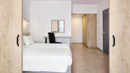 Hotellihuone, jossa on parivuode, kirjoituspöytä, peili ja säilytyskalusteet. (Tekoälyn luoma teksti)