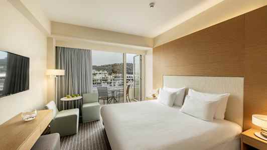 Hotellihuone, jossa on parivuode, istuinalue ja parveke näkymällä. (Tekoälyn luoma teksti)