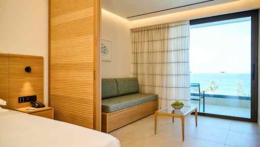 Modernisti sisustettu hotellihuone, jossa on sohva, pieni pöytä ja parveke merinäköalalla. (Tekoälyn luoma teksti)