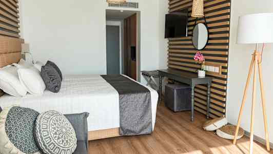 Tyylikäs hotellihuone, jossa on sänky, koristeellisia tyynyjä ja työpöytä. (Tekoälyn luoma teksti)