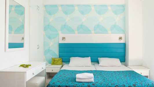 Hotellihuone, jossa kaksi sänkyä, siniset päälliset ja valkoinen sisustus. (Tekoälyn luoma teksti)