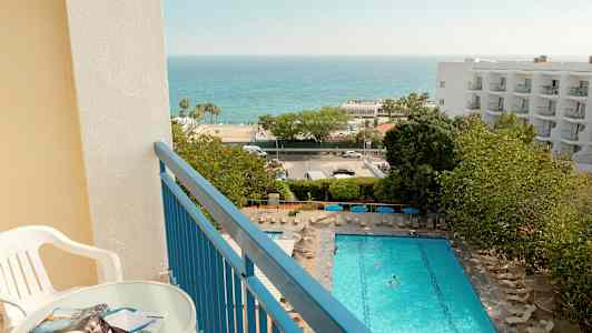 Näkymä parvekkeelta, jossa on pöytä ja tuoli, uima-altaalle, vihreään alueeseen ja merelle. (Tekoälyn luoma teksti)