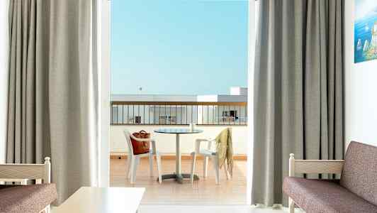 Hotellihuone, josta on näkymä parvekkeelle, jossa on pöytä ja tuolit. (Tekoälyn luoma teksti)