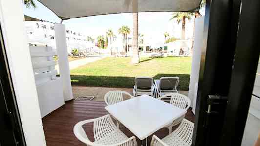 Terassi, jolla on pöytä ja tuolit, näkymä viheralueelle, jossa aurinkotuoleja. (Tekoälyn luoma teksti)