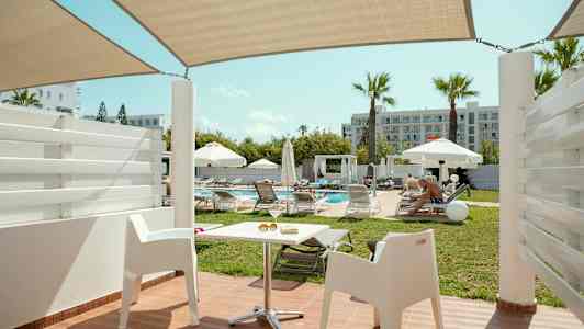 Näkymä terassilta valkoiset tuolit ja uima-allas, ympärillä aurinkotuoleja ja varjoja. (Tekoälyn luoma teksti)