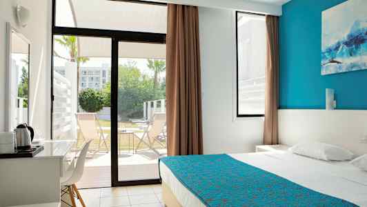 Moderni hotellihuone, jossa sininen päiväpeite, ikkuna avautuu terassille ja tuoleille. (Tekoälyn luoma teksti)