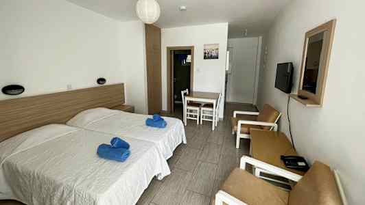 Hotellihuone, jossa on kaksi erillistä vuodetta, pöytä tuoleineen ja sohva. (Tekoälyn luoma teksti)