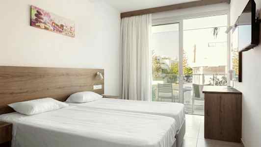 Kahden hengen huone, jossa kaksi erillistä vuodetta, lasiovi parvekkeelle ja seinälle kiinnitetty televisio. (Tekoälyn luoma teksti)