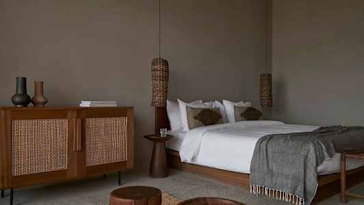 Makuuhuone, jossa suuri sänky, puinen pöytä ja rottinkityylinen lipasto. (Tekoälyn luoma teksti)