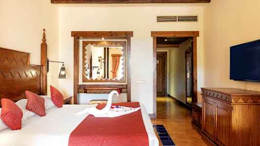 Hotellihuone, jossa parivuode, punaiset tyynyt ja sängyllä koriste, joka on muotoiltu joutseneksi. (Tekoälyn luoma teksti)