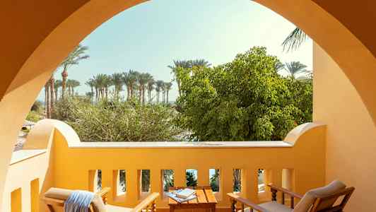 Parveke, jossa istuinkalusteet, edessä näkymä puihin ja palmuihin. (Tekoälyn luoma teksti)