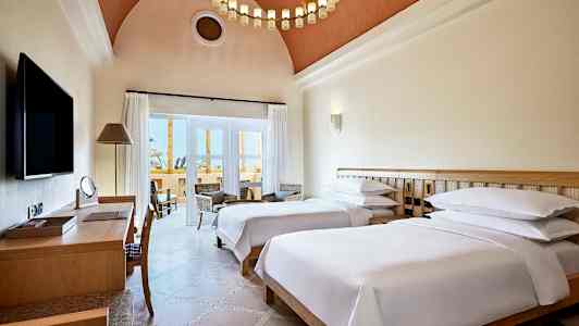 Hotellihuone, jossa on kaksi erillistä vuodetta, kirjoituspöytä ja oleskelutila parvekkeen vieressä. (Tekoälyn luoma teksti)