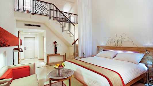 Modernisti sisustettu hotellisviitti, jossa on parivuode, istuinryhmä ja portaat avotilaan. (Tekoälyn luoma teksti)