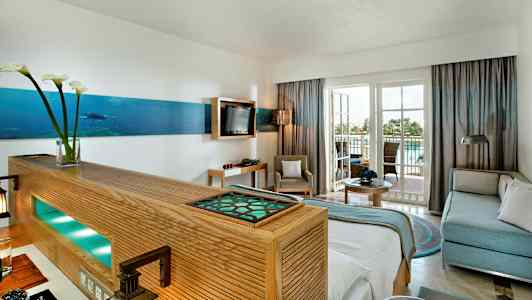 Vaalean hotellihuoneen sisustus, jossa istuinryhmä ja parveke. (Tekoälyn luoma teksti)