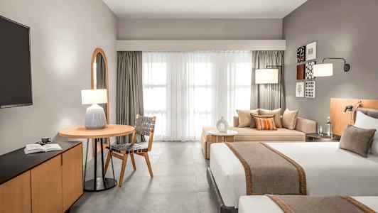 Moderni hotellihuone, jossa kaksi sänkyä, oleskelutila ja pöytä. (Tekoälyn luoma teksti)