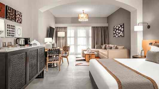 Hotellihuone, jossa on sänky, istuinryhmä ja ruokapöytä, sekä moderni sisustus. (Tekoälyn luoma teksti)