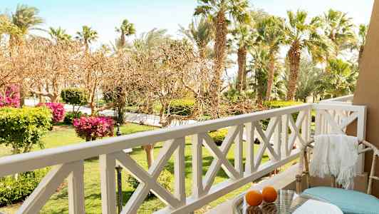 Näkymä parvekkeelta, jossa ulkokalusteet, pöytä ja appelsiineja, taustalla puutarha ja palmuja. (Tekoälyn luoma teksti)