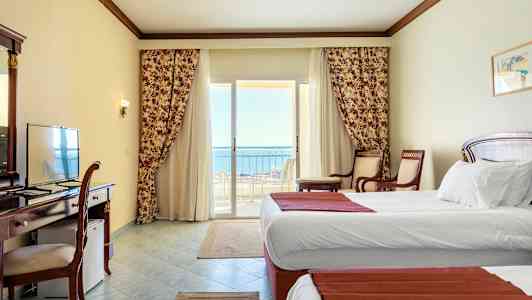 Hotellihuone, jossa on valkoiset seinät, kaksi yhden hengen vuodetta ja parveke merinäköalalla. (Tekoälyn luoma teksti)