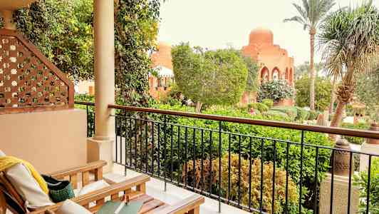 Terassi, jolla on puiset tuolit ja näkymä vehreään puutarhaan ja kupolilla varustettuun rakennukseen. (Tekoälyn luoma teksti)