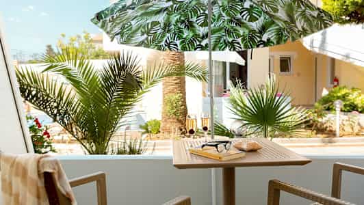 Parveke, jossa on varjo, pöytä, tuolit ja ulkokasvillisuutta. (Tekoälyn luoma teksti)