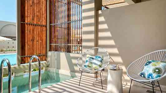 Kaksi tuolia, joissa on tyynyt, istuu pienen uima-altaan äärellä lähellä puupaneeleja. (Tekoälyn luoma teksti)