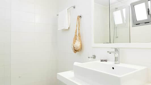 Vaalea kylpyhuone, jossa on valkoinen kaakeliseinä, pesuallas, pyyheteline ja peili. (Tekoälyn luoma teksti)