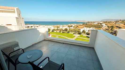 Terassi, jossa kaksi tuolia ja pöytä, sekä näkymät merelle ja asuinalueelle. (Tekoälyn luoma teksti)