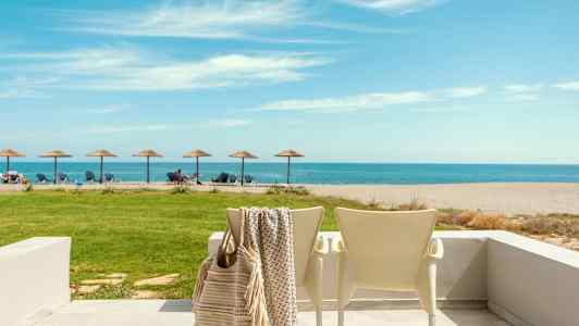 Ranta aurinkotuoleineen ja -varjoineen, taustalla meri, etualalla terassi tuoleineen. (Tekoälyn luoma teksti)