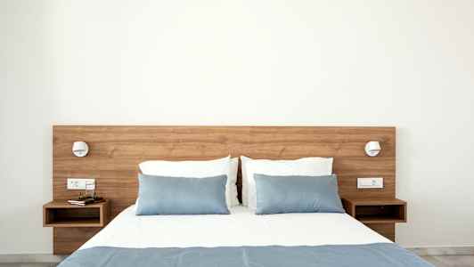 Sänky sinisellä päiväpeitteellä ja tyynyillä, puupöydät molemmilla puolilla. (Tekoälyn luoma teksti)