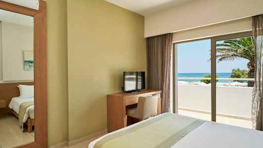 Hotellihuone, jossa on sänky, TV ja työpöytä, näkymä merelle ikkunan kautta. (Tekoälyn luoma teksti)