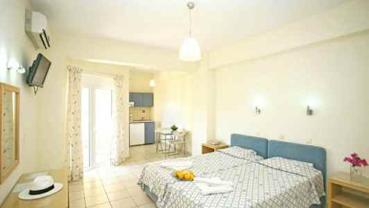 Valoisa huone, jossa on kaksi erillistä sänkyä, keittiö nurkassa ja lasiovi, joka johtaa parvekkeelle. (Tekoälyn luoma teksti)