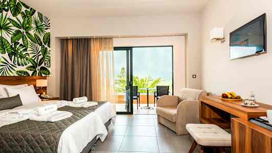 Hotellihuone, jossa on parivuode, istuinryhmä, parveke ja lehtikuvioitu seinäkoriste. (Tekoälyn luoma teksti)