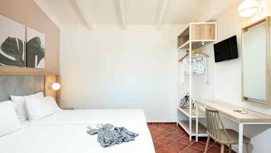 Hotellihuone, jossa parisänky, kirjoituspöytä, tuoli ja avoin vaateteline. (Tekoälyn luoma teksti)