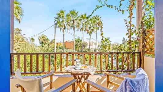 Parveke, jossa kaksi tuolia, pöytä ja näkymä palmupuihin. (Tekoälyn luoma teksti)