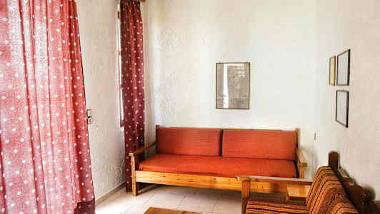 Olohuoneessa on punaiset verhot, puusohva punaisilla ruudullisilla tyynyillä ja kangaspäällysteinen tuoli vieressä. (Tekoälyn luoma teksti)