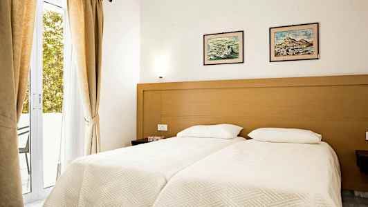 Makuuhuone, jossa kaksi erillistä sänkyä, puinen kehys, vaaleat lakanat ja kaksi taulua sänkyjen yläpuolella. (Tekoälyn luoma teksti)