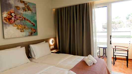 Hotellihuone, jossa kaksi erillistä vuodetta, seinällä taidemaalaus sekä lasiovet, jotka johtavat parvekkeelle pöydän ja tuolien kanssa. (Tekoälyn luoma teksti)