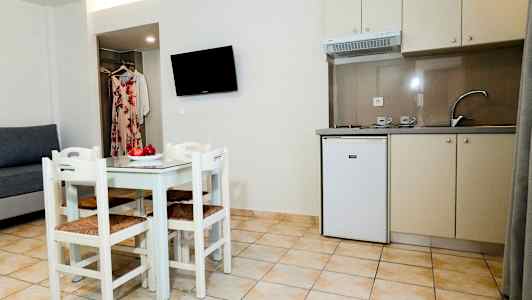 Pieni keittiö, jossa tiskiallas, jääkaappi ja ruokapöytä neljällä tuolilla sekä sohva ja seinään kiinnitetty TV. (Tekoälyn luoma teksti)