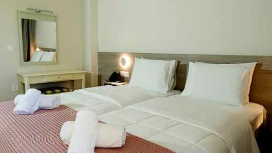 Kaksi yhden hengen vuodetta, joissa on valkoiset vuodevaatteet ja vaaleanpunaiset päiväpeitteet sekä valkoiset rullatut pyyhkeet päällä. (Tekoälyn luoma teksti)