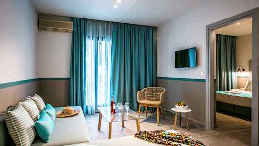 Kuva hotellihuoneesta, jossa on sohva, pöytä ja tuoli sekä makuuhuone erillisessä huoneessa. (Tekoälyn luoma teksti)