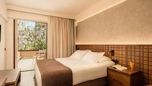 Hotellihuone, jossa on parivuode ja lasiovi, joka johtaa kalustetulle parvekkeelle. (Tekoälyn luoma teksti)